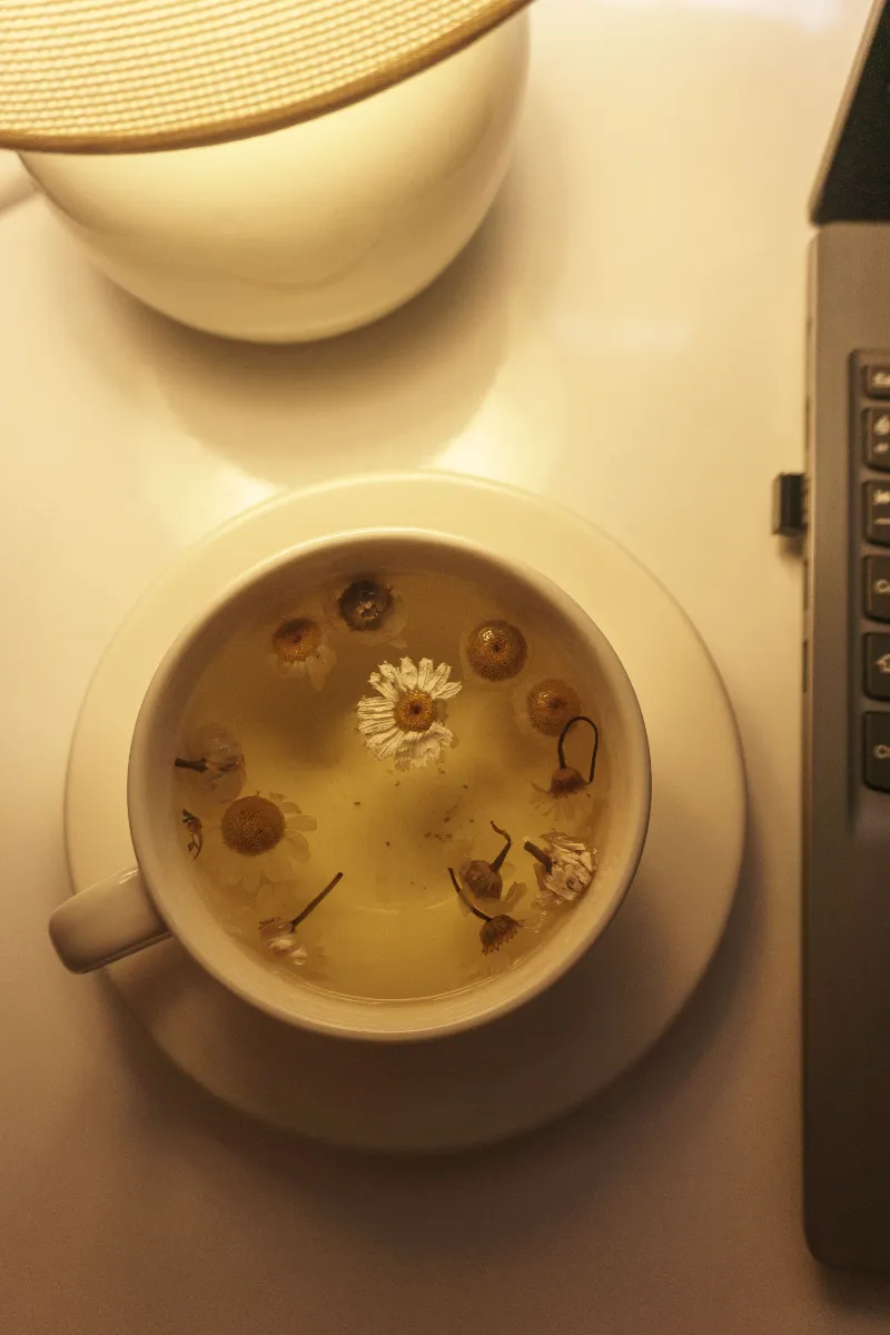 Taza de infusión de manzanilla con flores secas sobre una mesa de madera