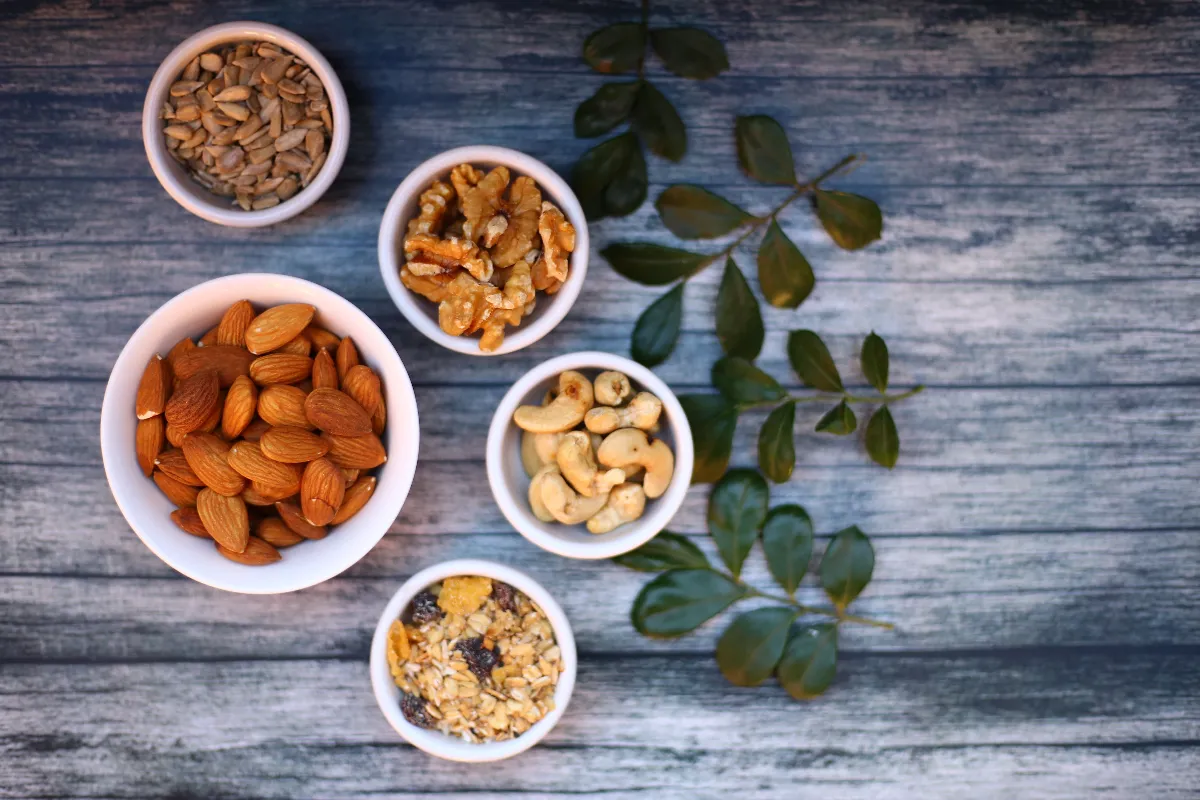 Frutos secos, semillas, espinacas y suplemento de magnesio sobre una mesa, representando alimentos ricos en magnesio y su relación con bienestar, calambres y sueño.