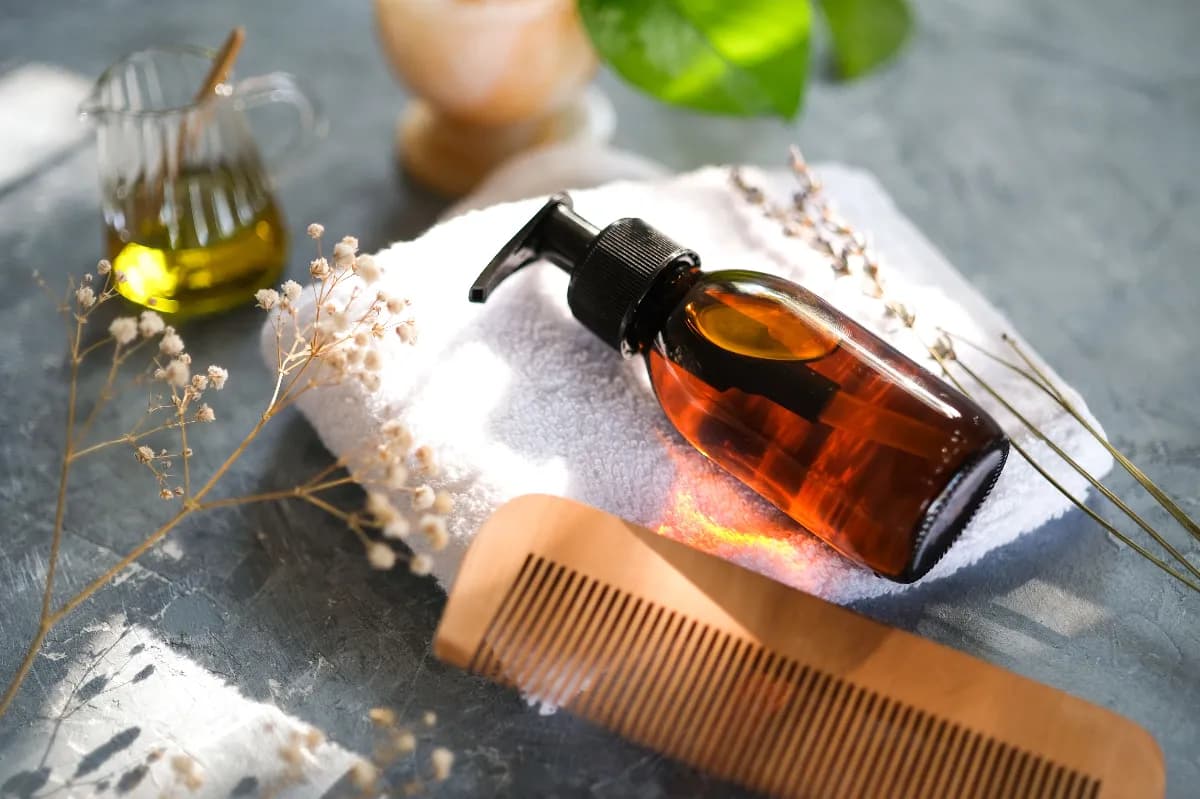 Frascos de aceites naturales para el cabello como coco, argán, jojoba y romero junto a un peine de madera y mechones de distintos tipos de pelo.